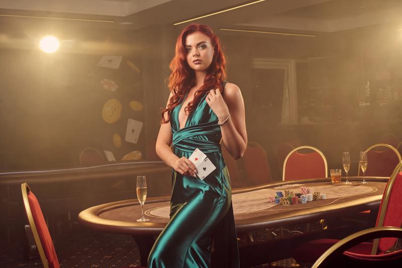 attractive-redheaded-maiden-long-blue-satin-dress-is-posing-sideways-with-two-aces-her-hand-against-poker-table-luxury-casino-passion-cards-chips-alcohol-win-gambling-it-is-as-fem